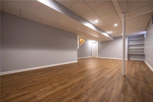 basement featuring a drop ceiling and dark wood-type flooring