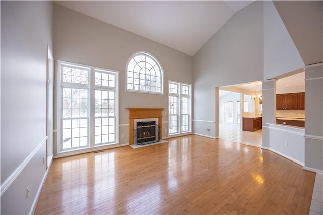 unfurnished living room featuring high vaulted ceiling, light hardwood / wood-style floors, decorative columns, and a notable chandelier