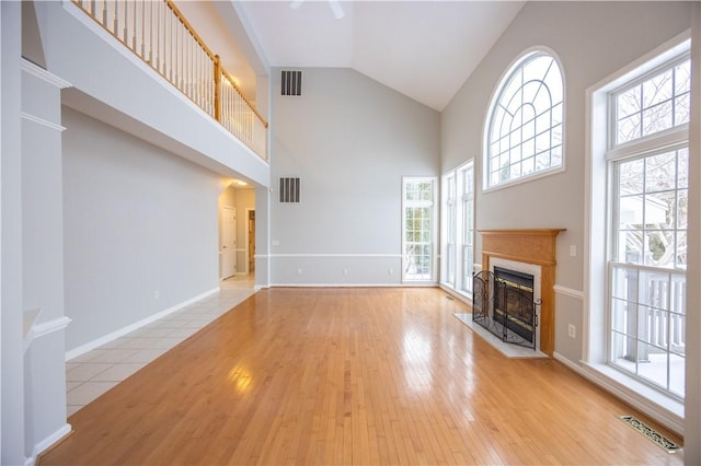 unfurnished living room with light hardwood / wood-style flooring, a high end fireplace, high vaulted ceiling, and plenty of natural light