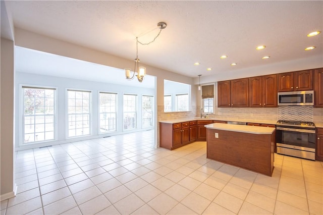 kitchen with appliances with stainless steel finishes, an inviting chandelier, hanging light fixtures, backsplash, and a center island