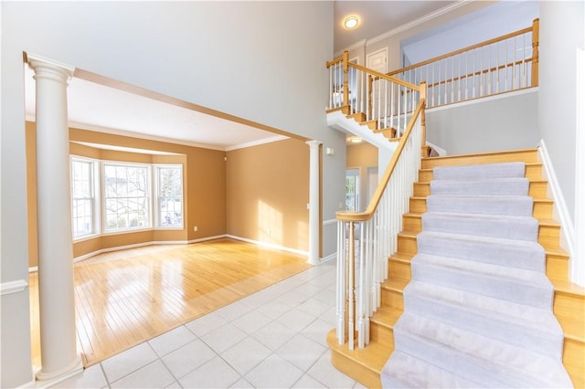 stairway featuring ornate columns, crown molding, a towering ceiling, and tile patterned flooring