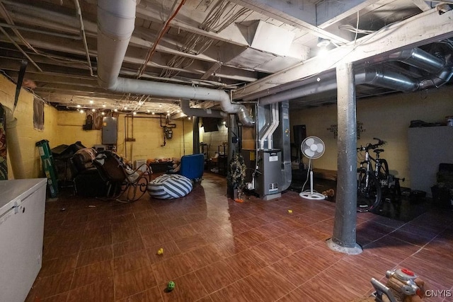 basement featuring fridge, heating unit, and electric panel