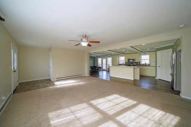 unfurnished living room with sink, a baseboard radiator, ceiling fan, and dark colored carpet