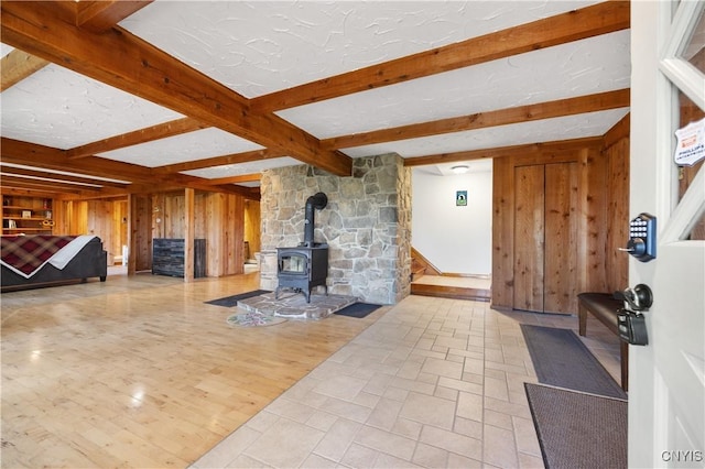 living room with beam ceiling, wooden walls, a textured ceiling, and a wood stove