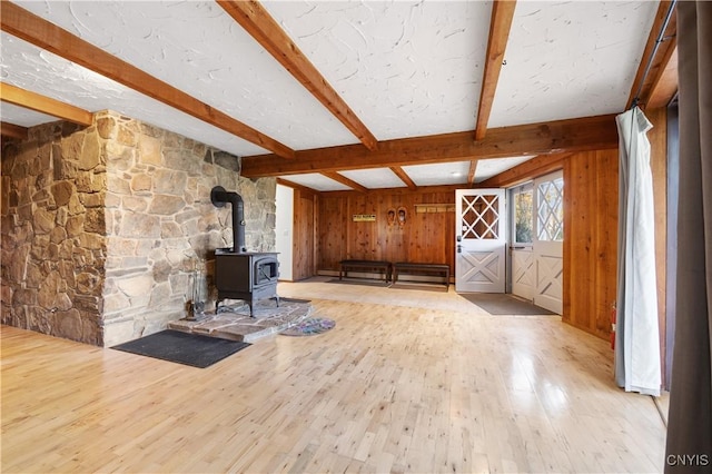 unfurnished living room featuring hardwood / wood-style floors, beam ceiling, and a wood stove