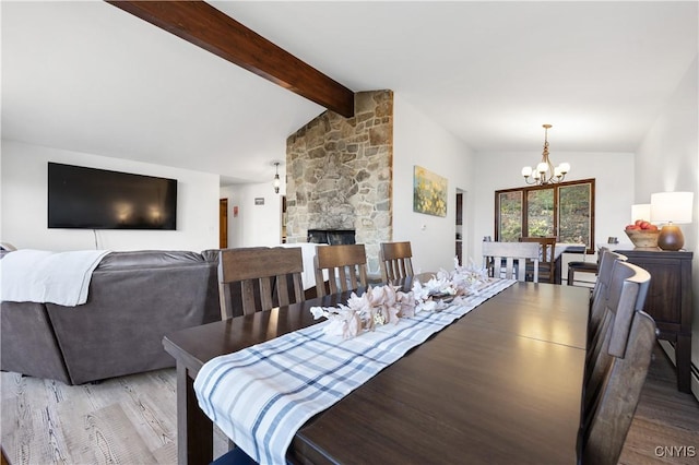 dining space with lofted ceiling with beams, a stone fireplace, a chandelier, and light hardwood / wood-style flooring