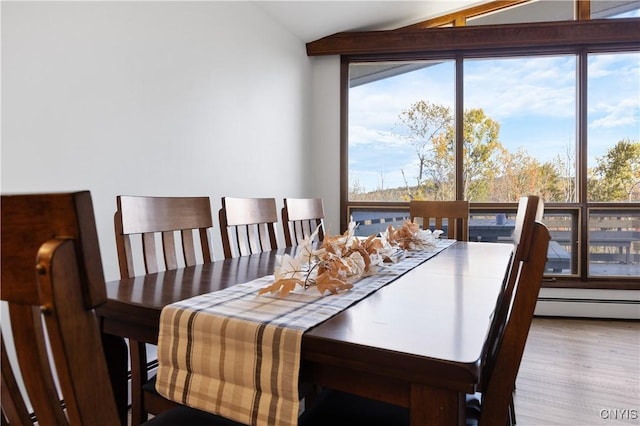 dining area with a baseboard heating unit, vaulted ceiling, and wood-type flooring