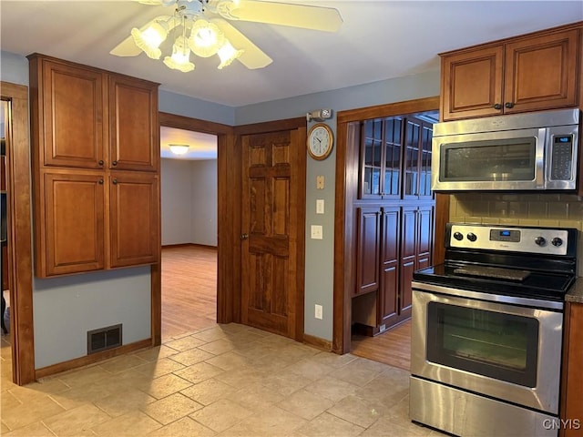 555 County Route 51, New Haven, NY 13114 - kitchen with appliances with stainless steel finishes, baseboards, backsplash, a ceiling fan, and brown cabinets