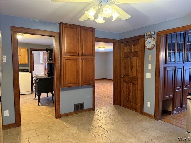 555 County Route 51, New Haven, NY 13114 - kitchen with washer / clothes dryer, a ceiling fan, baseboards, light stone finish flooring, and brown cabinets