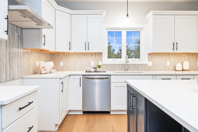 kitchen featuring sink, decorative light fixtures, stainless steel dishwasher, wall chimney range hood, and white cabinets