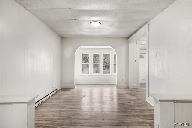 unfurnished living room with wood-type flooring, a baseboard heating unit, and a paneled ceiling