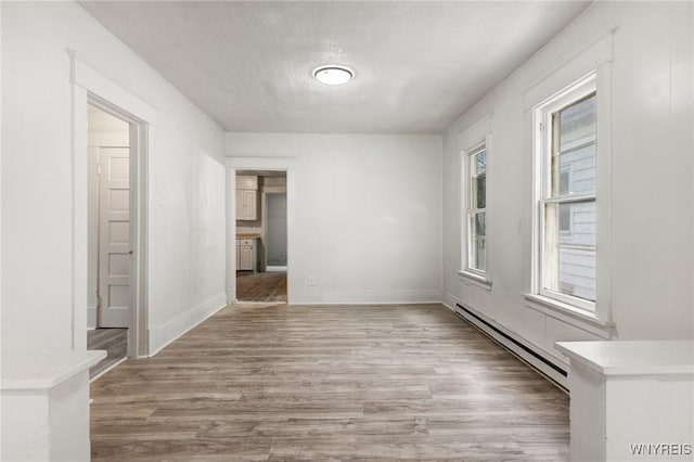 unfurnished room with a baseboard heating unit, a textured ceiling, and light hardwood / wood-style floors