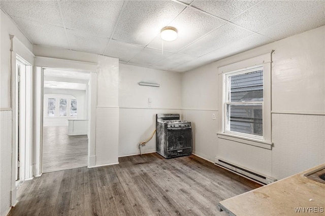 unfurnished room featuring hardwood / wood-style flooring, a baseboard radiator, a paneled ceiling, and tile walls