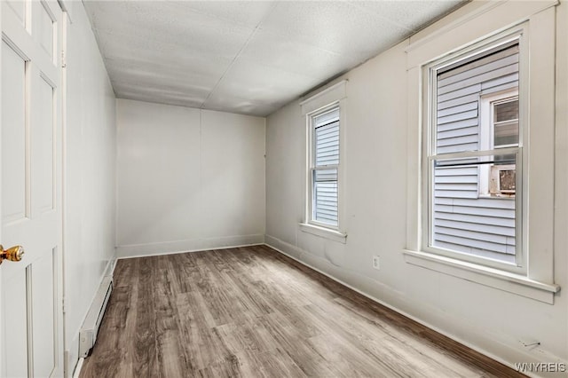 empty room with light wood-type flooring, a textured ceiling, and baseboard heating