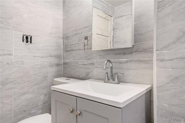 bathroom with vanity, tile walls, and toilet