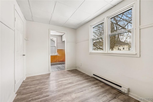 empty room with a baseboard heating unit, a paneled ceiling, and light wood-type flooring