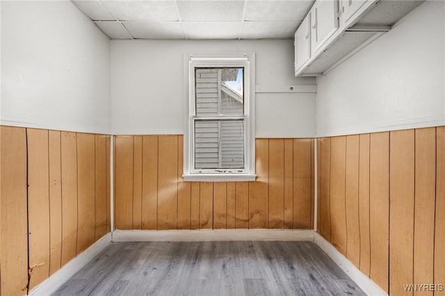 unfurnished room featuring a drop ceiling, light wood-type flooring, and wood walls