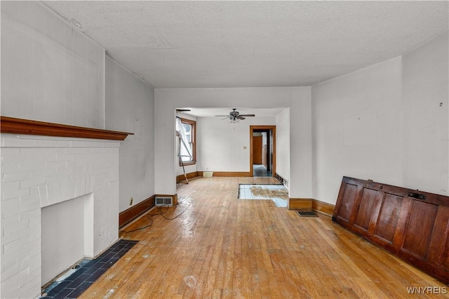 unfurnished living room with ceiling fan, a fireplace, light hardwood / wood-style floors, and a textured ceiling