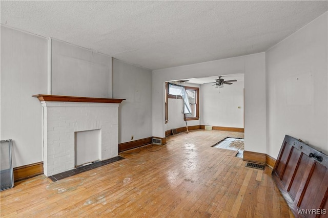 unfurnished living room featuring ceiling fan, light hardwood / wood-style floors, a brick fireplace, and a textured ceiling