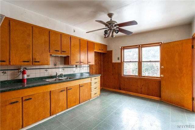 kitchen with ceiling fan, wood walls, sink, and backsplash