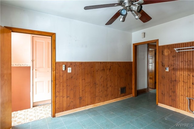 unfurnished room with ceiling fan and wooden walls