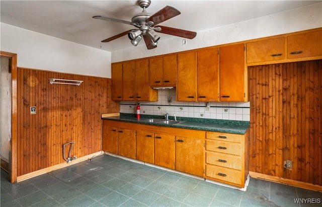 kitchen featuring sink, backsplash, wooden walls, and ceiling fan