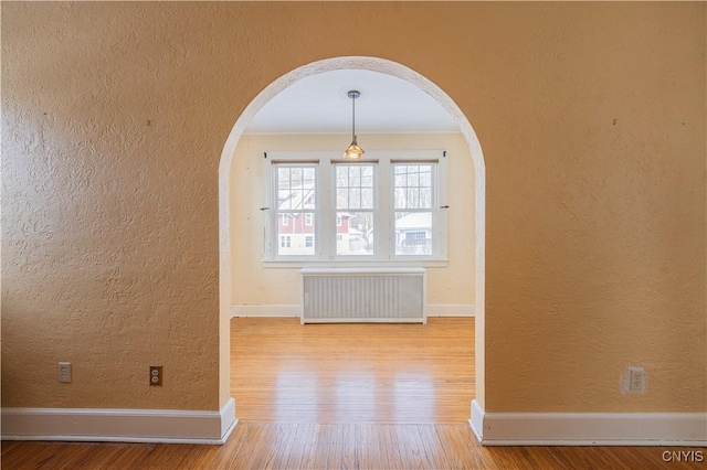 empty room with hardwood / wood-style flooring and radiator heating unit