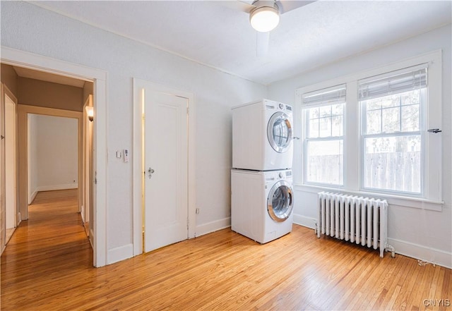 washroom with ceiling fan, stacked washer and clothes dryer, radiator heating unit, and light hardwood / wood-style floors