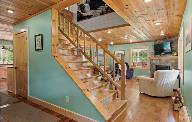 stairs featuring hardwood / wood-style flooring, a stone fireplace, and wooden ceiling