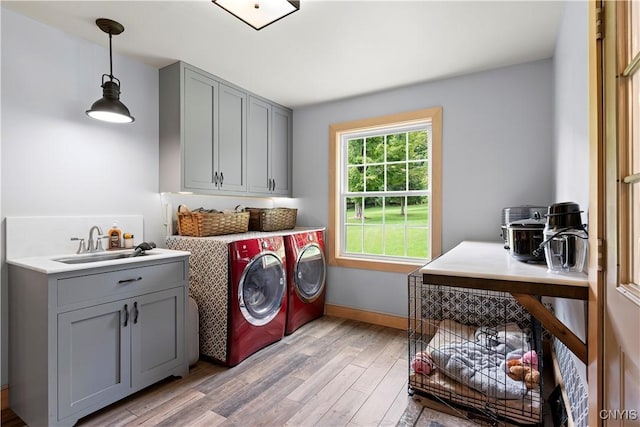 clothes washing area featuring cabinets, sink, washer and clothes dryer, and light hardwood / wood-style floors