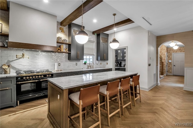 kitchen featuring a breakfast bar area, light stone counters, a kitchen island, light parquet flooring, and range with two ovens