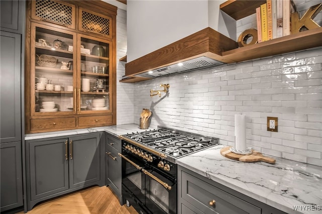 kitchen with light parquet floors, double oven range, light stone counters, and decorative backsplash