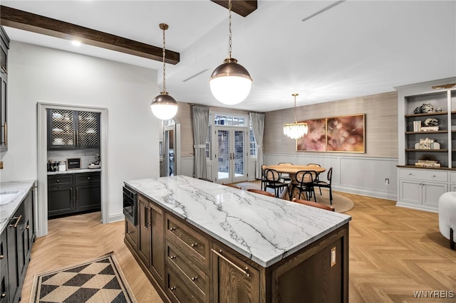 kitchen with a kitchen island, stainless steel microwave, decorative light fixtures, light stone counters, and light parquet flooring