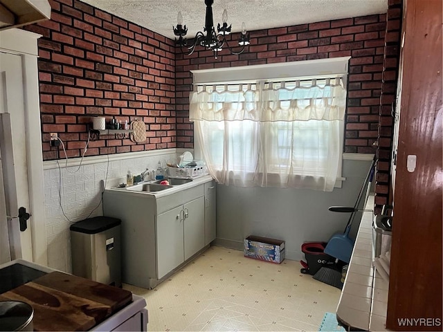 kitchen featuring brick wall, sink, white range, a notable chandelier, and a textured ceiling