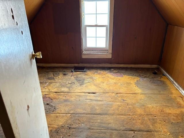 additional living space featuring vaulted ceiling and wood walls