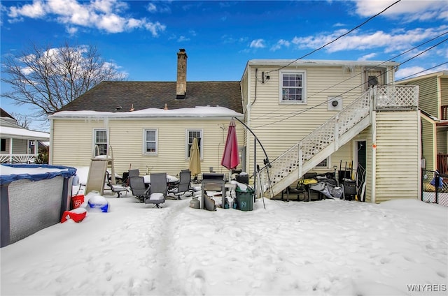 snow covered rear of property with a covered pool and an outdoor fire pit