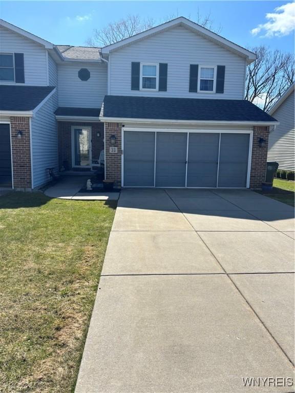 traditional home with an attached garage, concrete driveway, a front lawn, and brick siding