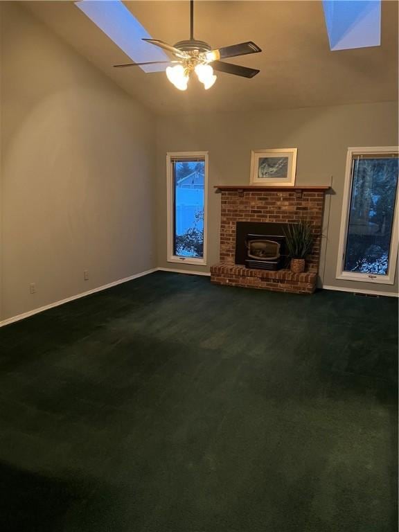 unfurnished living room with ceiling fan, vaulted ceiling with skylight, and dark carpet