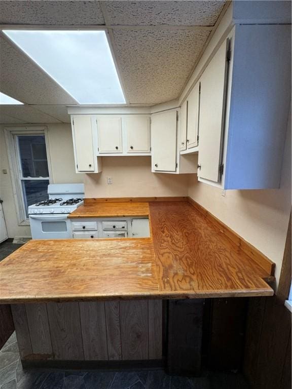 kitchen with a drop ceiling, white gas range, and white cabinetry