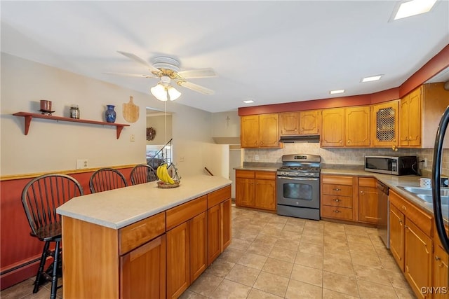 kitchen featuring backsplash, a kitchen breakfast bar, ceiling fan, stainless steel appliances, and a baseboard heating unit