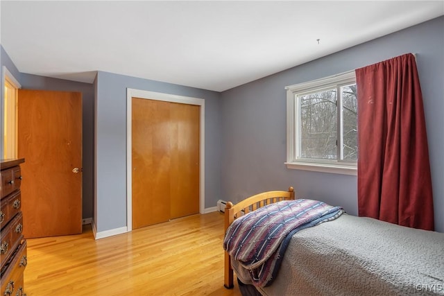 bedroom featuring a baseboard heating unit, light hardwood / wood-style floors, and a closet