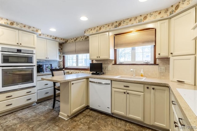 kitchen with sink, a breakfast bar area, white dishwasher, kitchen peninsula, and stainless steel double oven