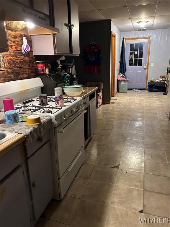 kitchen with a paneled ceiling, under cabinet range hood, and white gas range oven