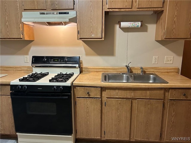 kitchen with light countertops, a sink, under cabinet range hood, and gas range