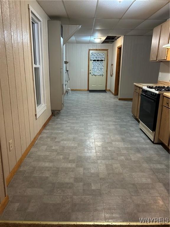 interior space featuring a paneled ceiling, wood walls, gas range oven, and baseboards