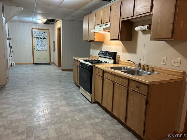 kitchen featuring range with gas stovetop, light countertops, a paneled ceiling, under cabinet range hood, and a sink