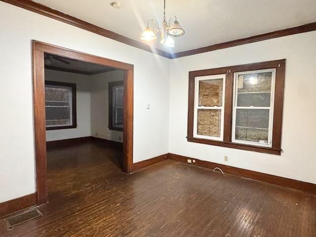 spare room featuring crown molding, dark wood-type flooring, and a notable chandelier