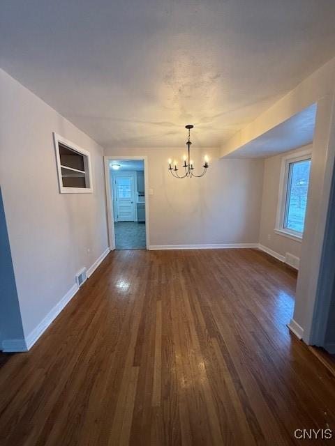 empty room with a notable chandelier and dark hardwood / wood-style floors