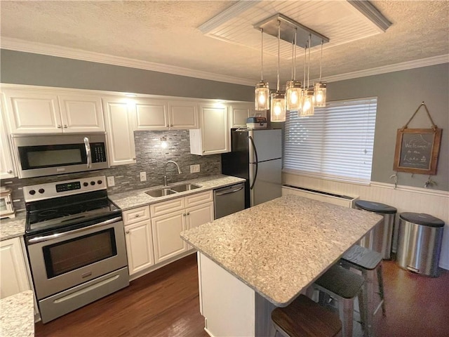 kitchen featuring appliances with stainless steel finishes, decorative light fixtures, white cabinetry, sink, and a kitchen breakfast bar