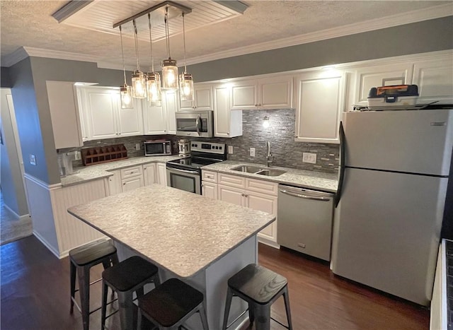 kitchen featuring sink, decorative light fixtures, a center island, stainless steel appliances, and white cabinets